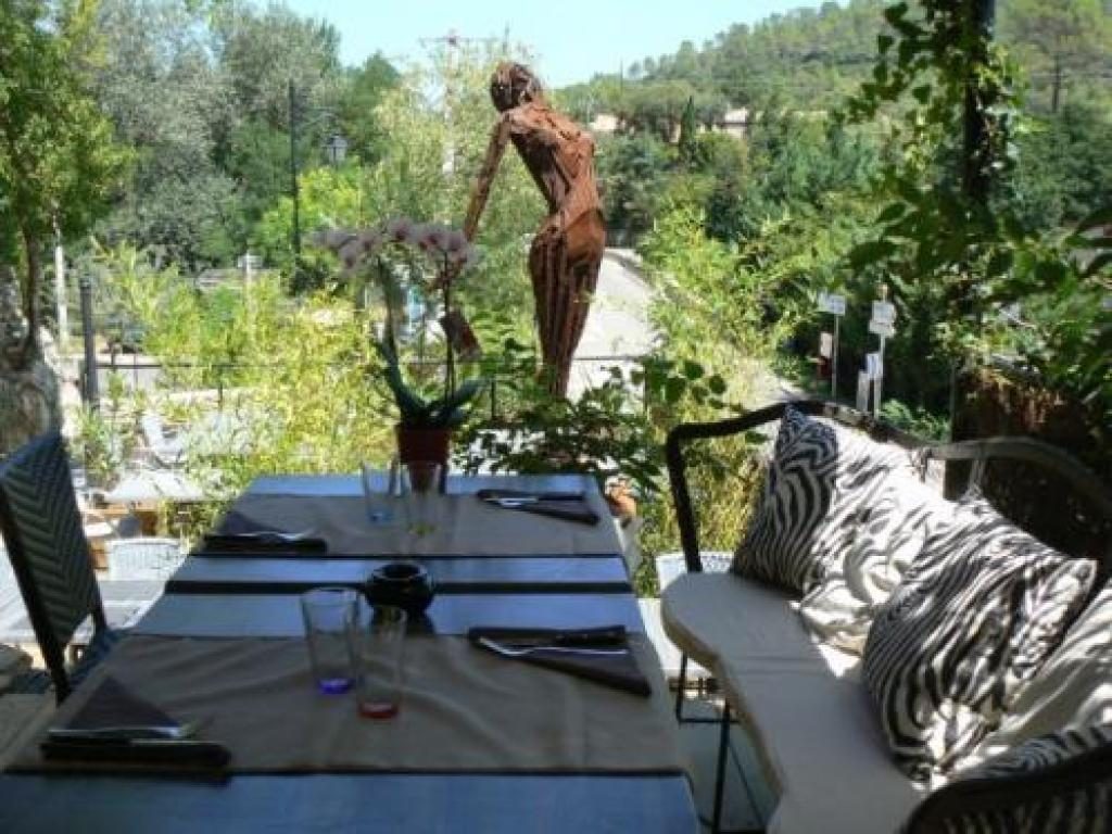 Une table dressée au bord de la terrasse, avec vue sur la verdure et une sculpture