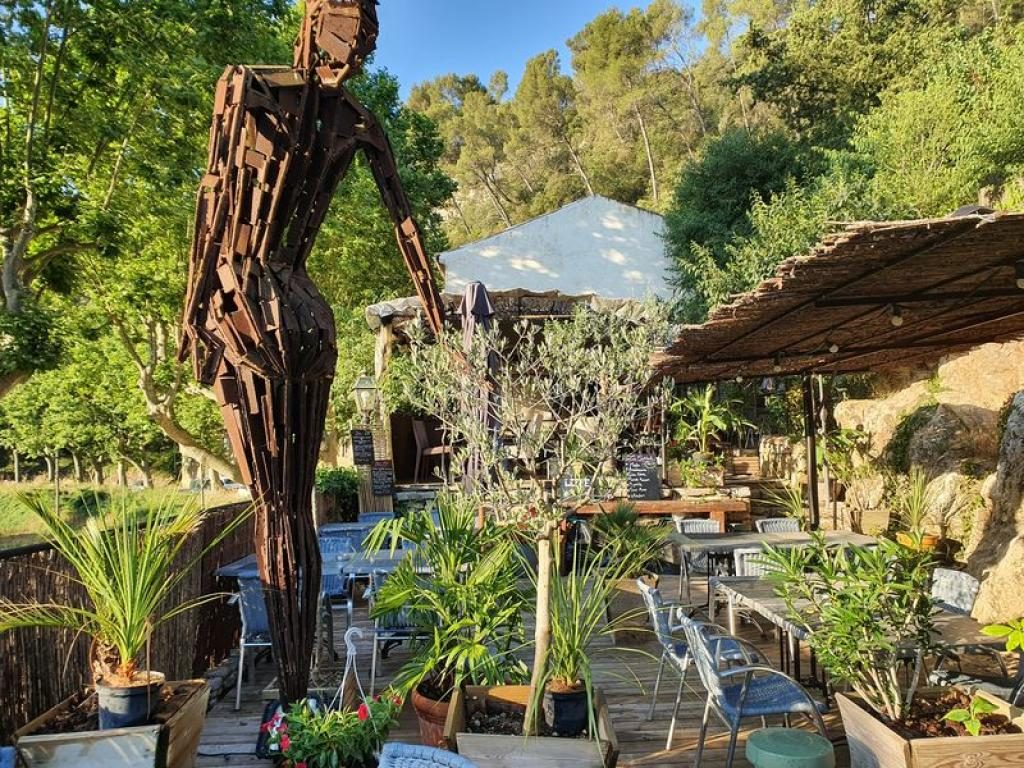 Une grande sculpture en bois au milieu des tables, sous les arbres